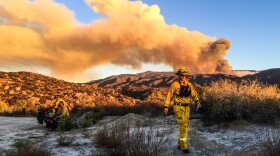 A firefighter is pictured in this undated photo as smoke from the Cutca Fire rises in the background.