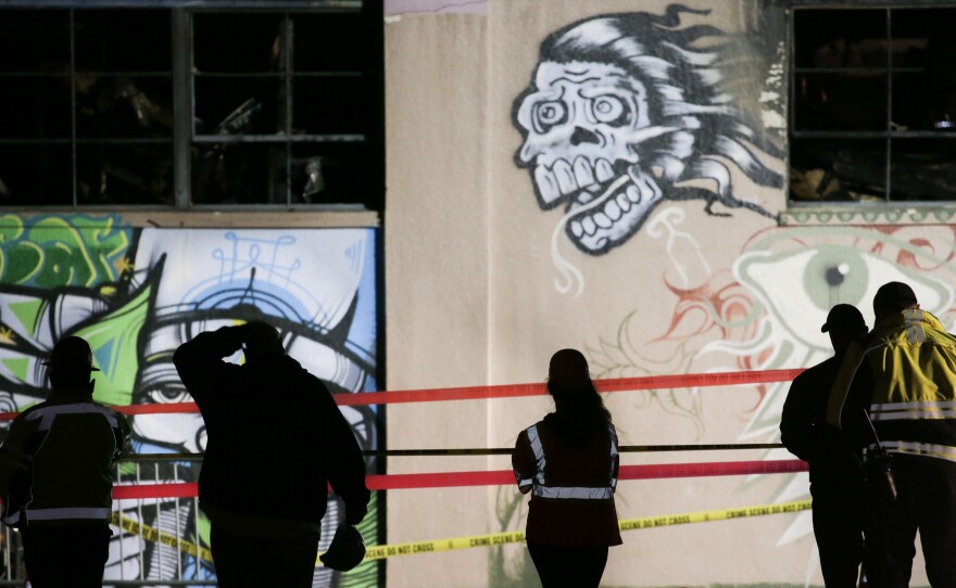 On Monday, workers and emergency responders look at a warehouse in which a fire late Friday claimed the lives of at least 36 people on in Oakland, Calif.