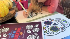 A young girl colors in the KPBS Dia de Muertos coloring book in San Diego County, Calif. Oct. 19, 2025.