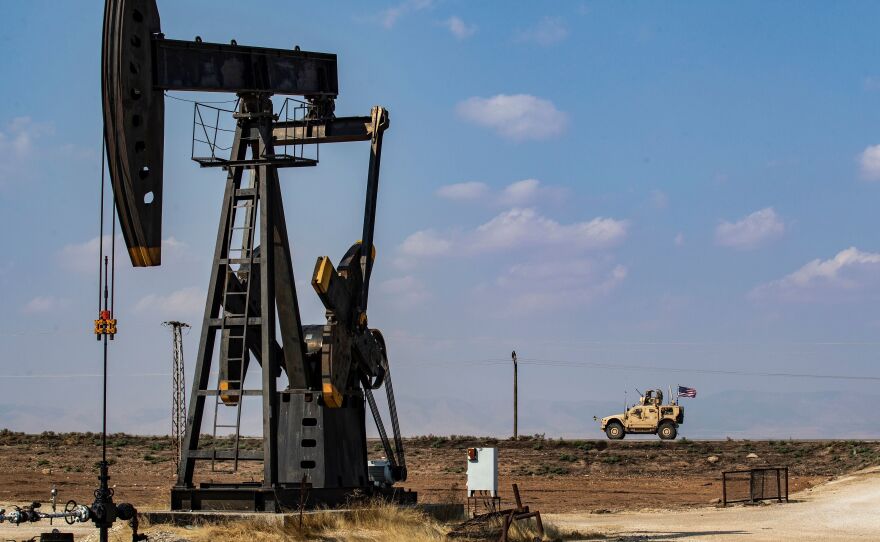 A U.S. military vehicle drives past an oil pump jack in the countryside of Syria's northeastern city of Qamishli. President Trump is leaving some U.S. troops in Syria, with the goal of controlling Syria's oil fields. But legal experts say exploiting the oil could amount to pillaging — a war crime.