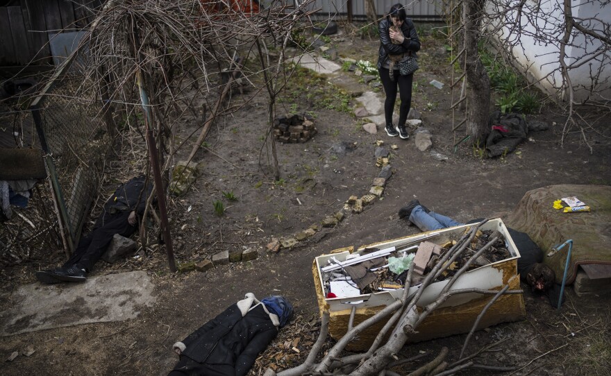 A woman walks with her cat next to the corpses of her husband and brother, killed in Bucha.