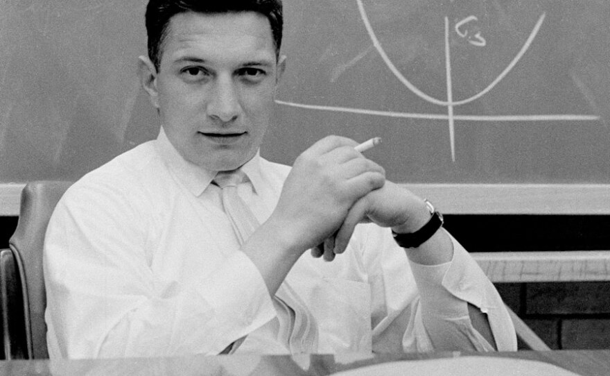 Robert Noyce seated at his desk in front of a diagram on a blackboard at Fairchild.