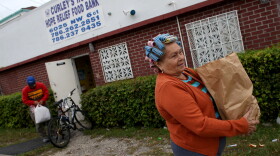 Elba Salsado walks with her groceries after receiving them from a food bank in Miami.
