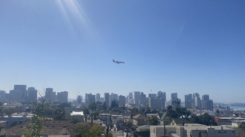 A plane flies over a sunny Downtown San Diego skyline on Feb. 27, 2021.