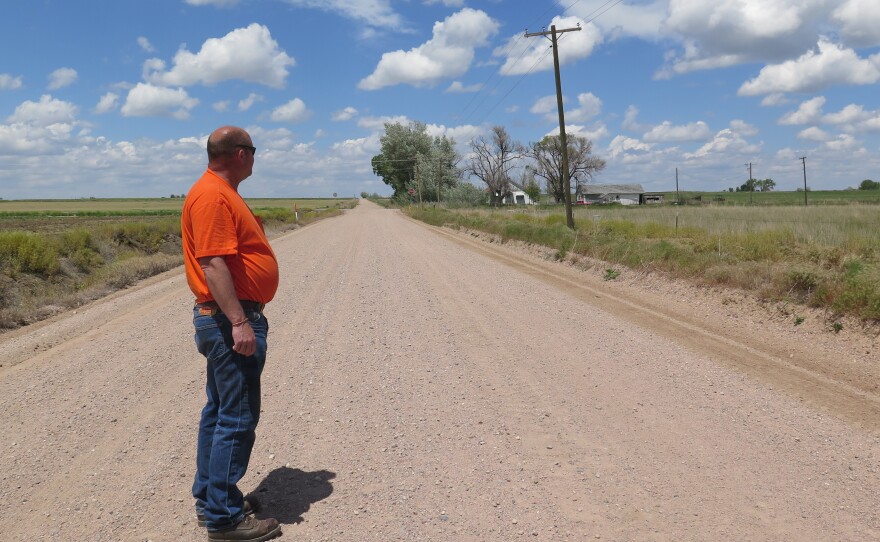 Ault Mayor Butch White stands on a road dividing two farms, one irrigated and one dried up.