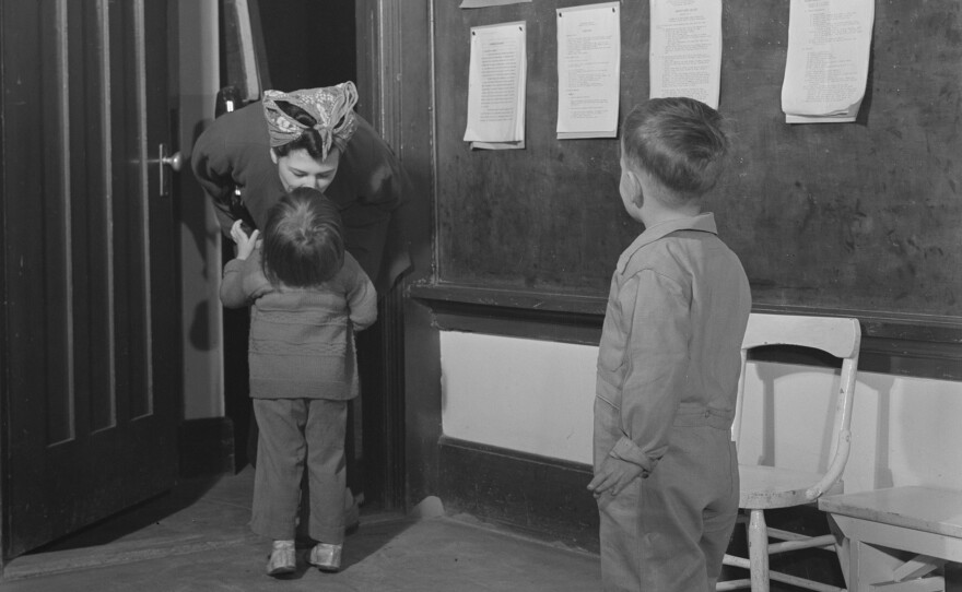 A woman in coveralls kisses her child goodbye (undated photo). "Women of World War II: The Untold Stories"