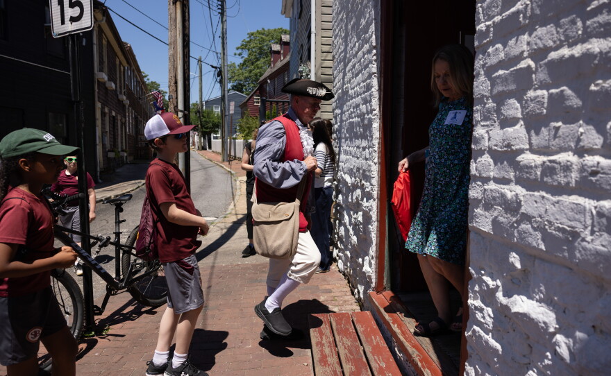 A reenactor dressed in Colonial-era garb enters Waterfront Warehouse with a group of schoolchildren in Annapolis.