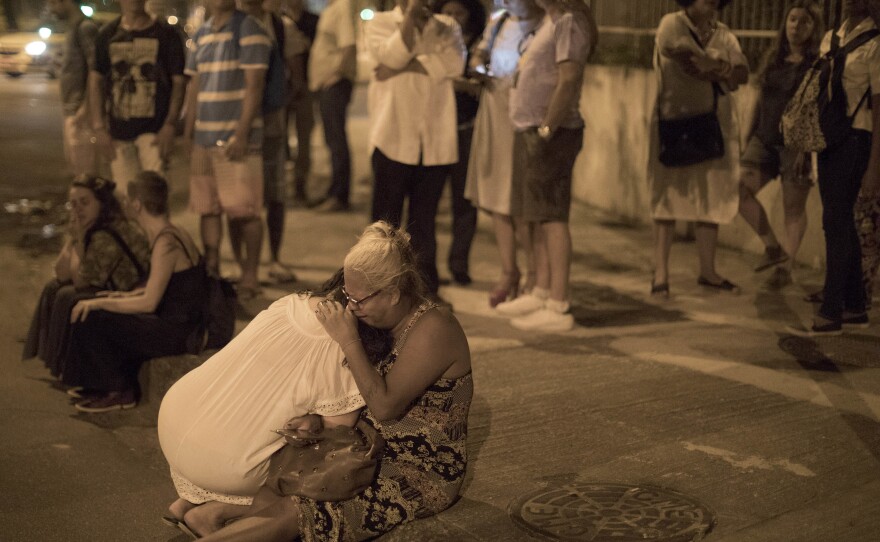 People cry on the sidewalk next to the scene where council member Marielle Franco and her driver were shot to death by two unidentified attackers in Rio de Janeiro on Thursday.