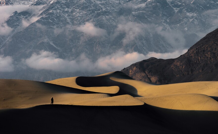 A man walks along a sand dune in the cold desert as a mountain looms in Skardu, Pakistan.