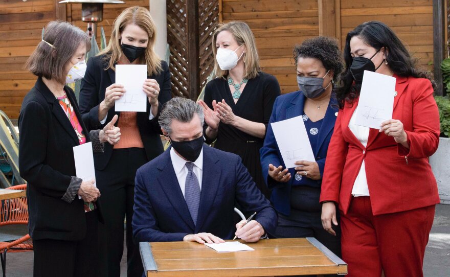 Gov. Gavin Newsom, center, signs legislation to extend COVID-19 supplemental paid sick leave for workers and bolster California's support for small businesses on Wednesday, Feb. 9, 2022, in Oakland, Calif.