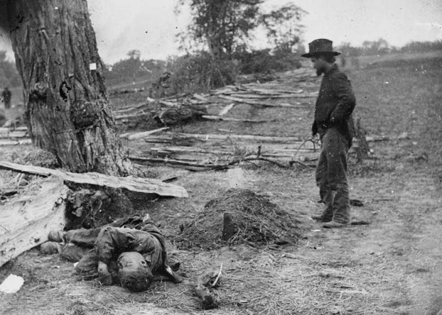 A soldier looking upon a Union soldier's grave with the body of a Confederate soldier seemingly tossed aside in Antietam, Maryland, September 1862.