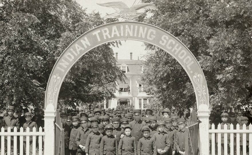 Boys in uniforms stand at gate to Chemawa Indian Training School.