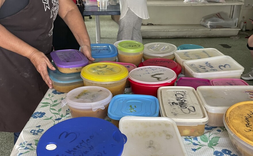 A volunteer fills up tupperware containers with beef stew.