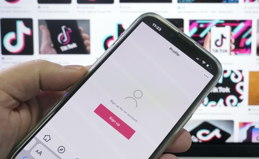A sign up page for the application TikTok is shown on a cell phone in front of a screen with logos for the company in Sydney, Tuesday, April 4, 2023.