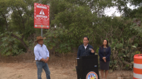 County Supervisor Paloma Aguirre, right, and San Diego Mayor Todd Gloria, center, unveil new Tijuana sewage "warning" signs. Resident Gabriel Uribe, left, says exposure to toxic gas stemming from the polluted Tijuana River has affected his health.