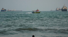 A swimmer remains near the shore as a motorboat passes commercial vessels anchored in the Strait of Hormuz off Bandar Abbas, Iran, on Friday.