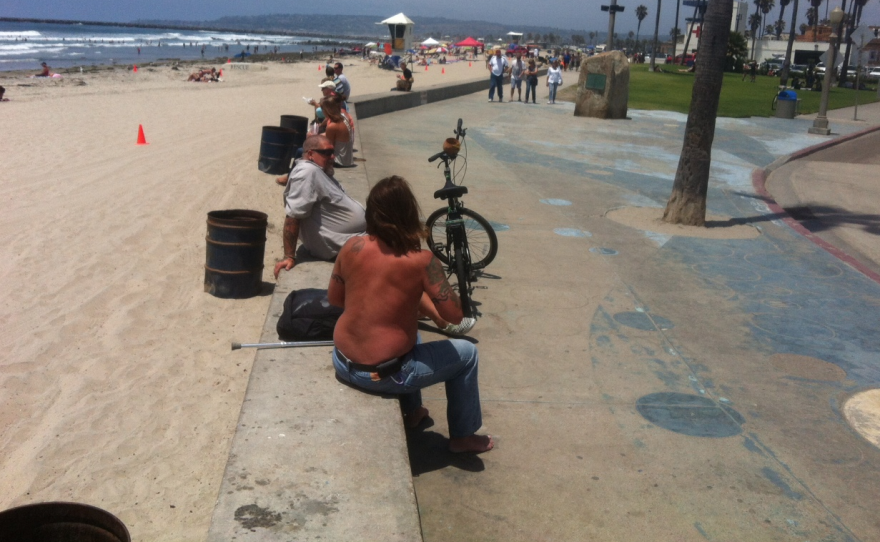 Beachgoers sit on the concrete wall that separates the sand from the sidewalk along Newport Avenue in Ocean Beach, June 26, 2014.