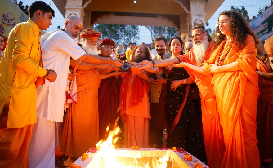 Pujya Swami Chidanand Saraswatiji, center, and Sadhvi Bhagawati Saraswati, far right, join other faith leaders in the <em>yagna, </em>a fire ceremony meant to purify the mind and air, at their ashram beside the flowing Ganges. It precedes the Ganga Aarti, a ritual to show reverence to the river.