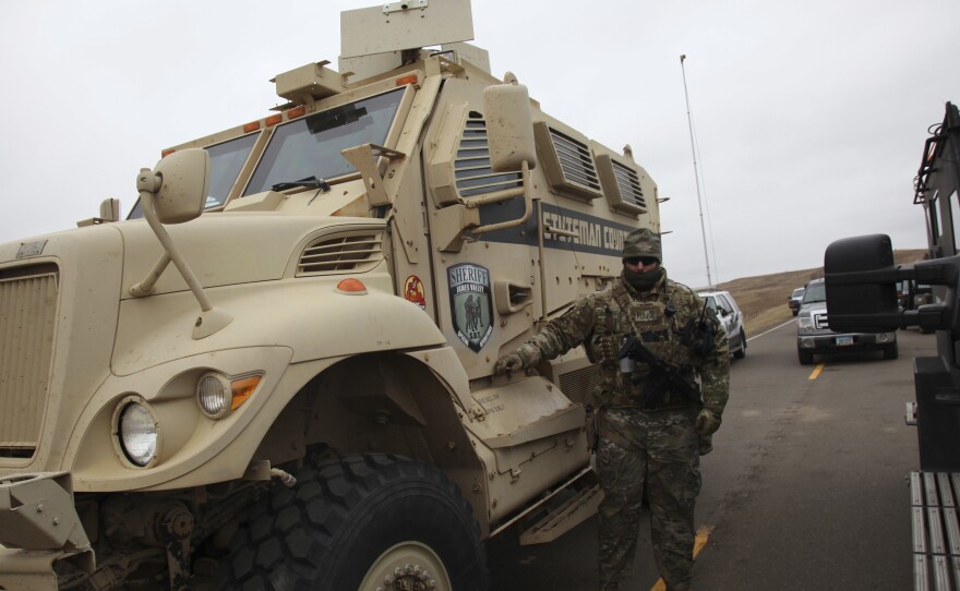 A member of the Stutsman County SWAT team who declined to give his name nor to be identifiable by badge stands guard by an armored personnel carrier equipped with an LRAD, or long range acoustic device, while deployed to watch protesters demonstrating against the Dakota Access Pipeline.