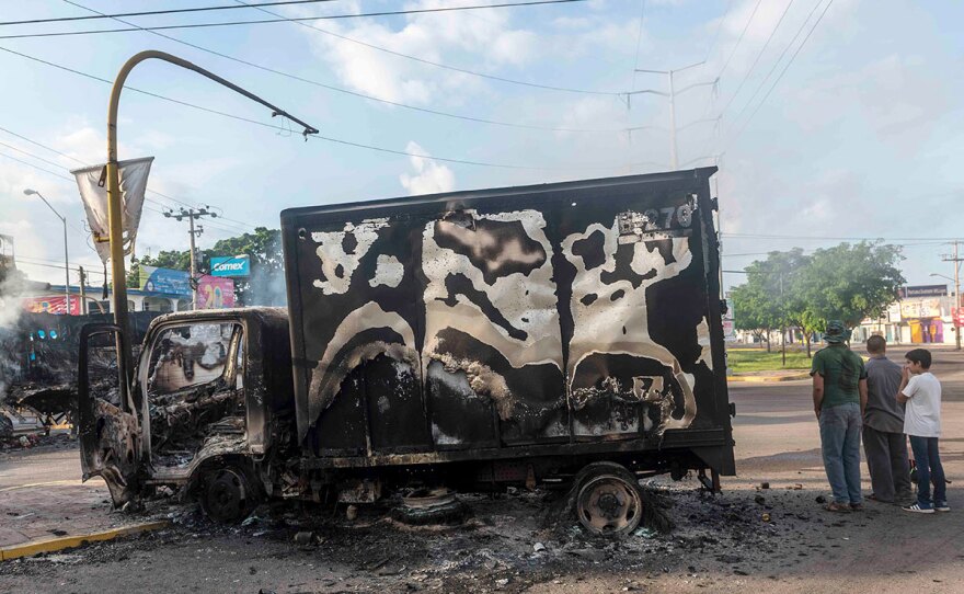 A burnt out truck used by gunmen smoldering on an intersection, a day after street battles between gunmen and security forces in Culiacan, Mexico,  Oct. 18, 2019.