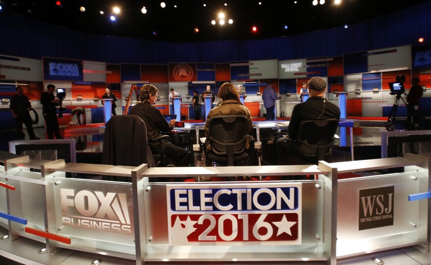 Workers stand in at the candidate's podiums Monday, Nov. 9, 2015, in preparation of for Tuesday's Republican debate in Milwaukee.