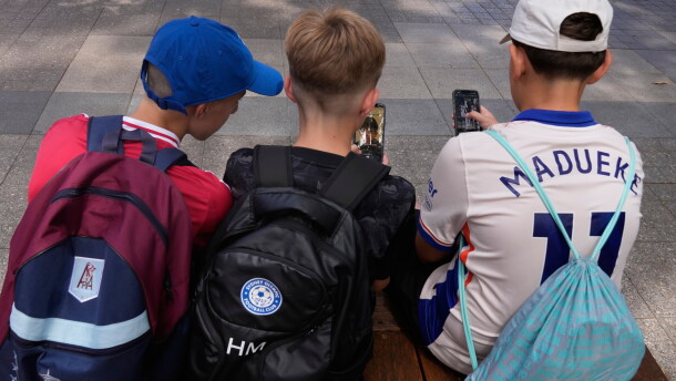 FILE - Three boys use their phones while sitting outside a school in Sydney, Monday, Dec. 8, 2025.