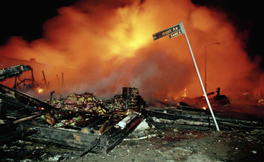 The remains of a commercial building smoulders as another building burns out of control behind the smoke in Los Angeles early on the morning of April 30, 1992.