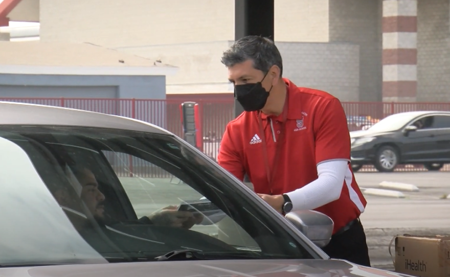 A Sweetwater High School staff member distributes a COVID-19 testing kit to a parent in the Sweetwater High School parking lot on January 7, 2022.