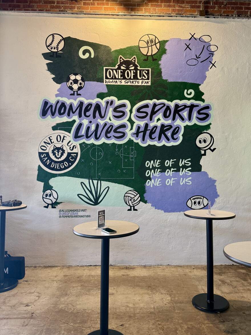 A mural designed by FemmeFolio Design Studio and painted by Allison Hunsley serves as the centerpiece of a standing-room-only area of One of Us in North Park on July 22, 2026.