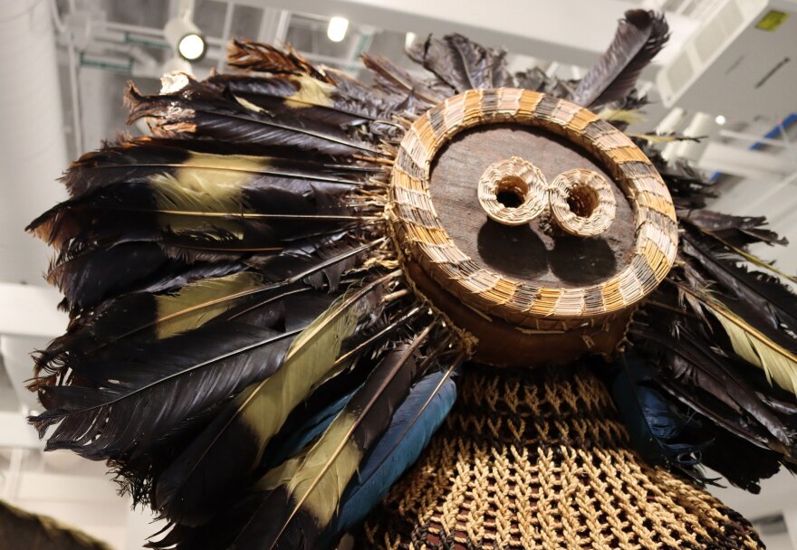 At the entrance of the exhibition is a Gitenga mask, a circular "face" with two large eyes, shown in a Jan. 2023 photo. Feathers radiate out around the face, like a sun. A Gitenga mask could be used in multiple ways, whether as an initiation or induction ritual. Displayed in the gallery, the mask's pedestal is transformed into a body, wearing a raffia costume.