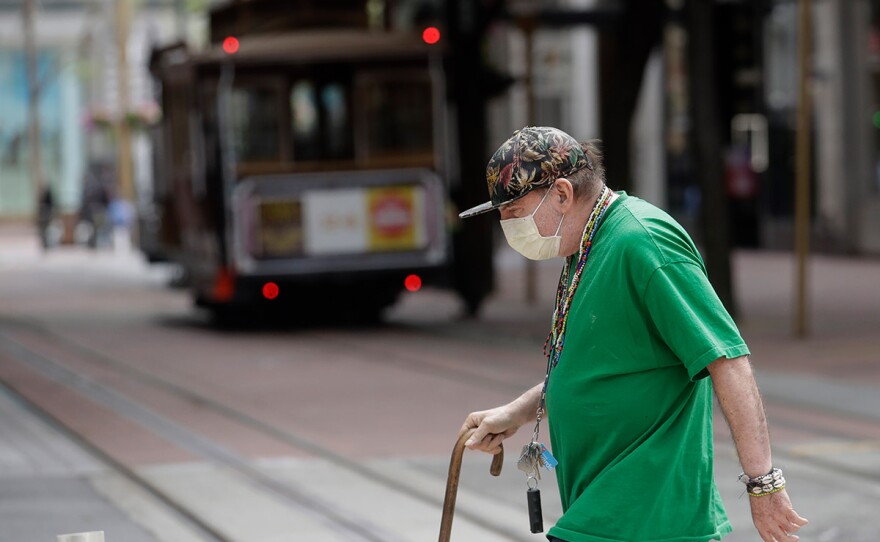 A man wears a mask while crossing a street in front of a Cable Car in San Francisco, Sunday, March 15, 2020.