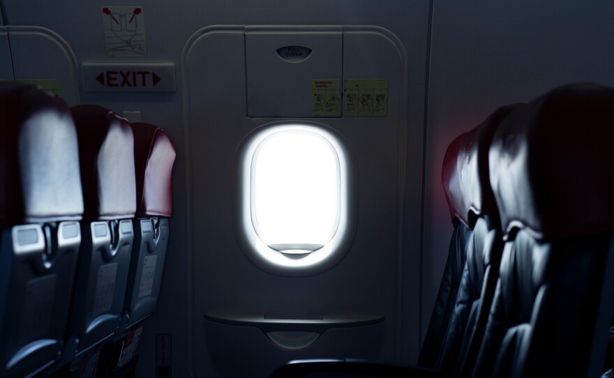 Where should you sit on a plane to reduce the risk of exposure to germs spread by infectious passengers?