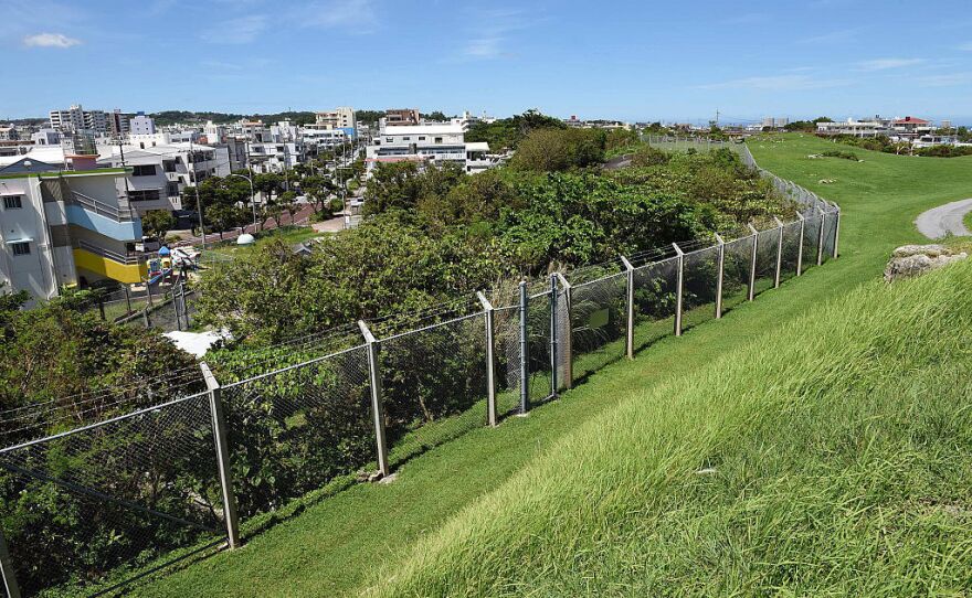 Beyond the barbed-wire fence at Marine Corps Air Station Futenma, Okinawans live in the dense building construction of Ginowan, where the city has grown around the military installation.