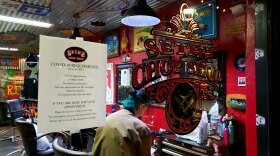 A woman sitting inside Seth's Chop Shop hair salon in Ocean Beach on May 29, 2020, with a sign displaying COVID-19 safety measures.