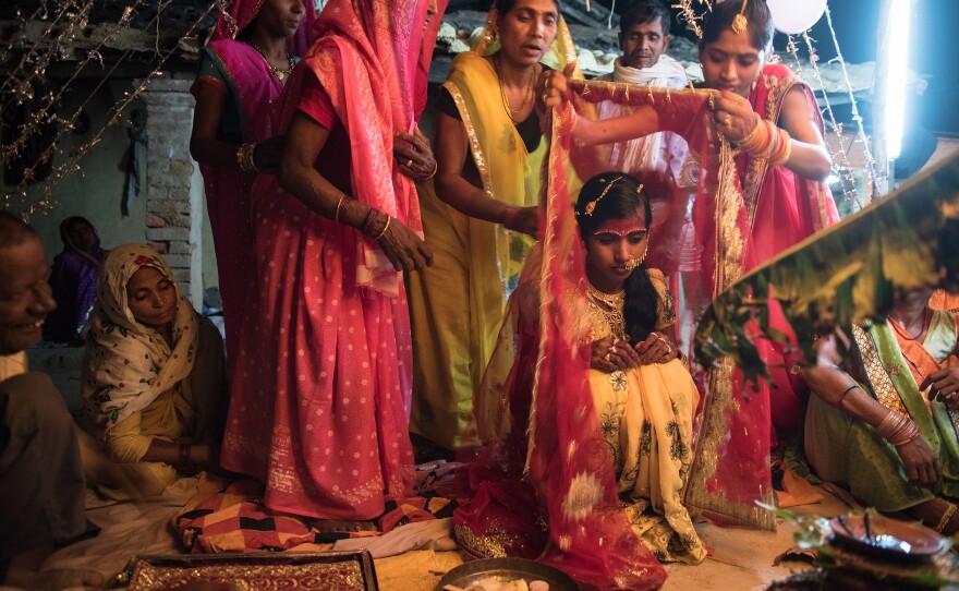 The 14-year-old bride is draped in a red cloth as she waits for the groom to arrive for the wedding rituals in the courtyard of her house.