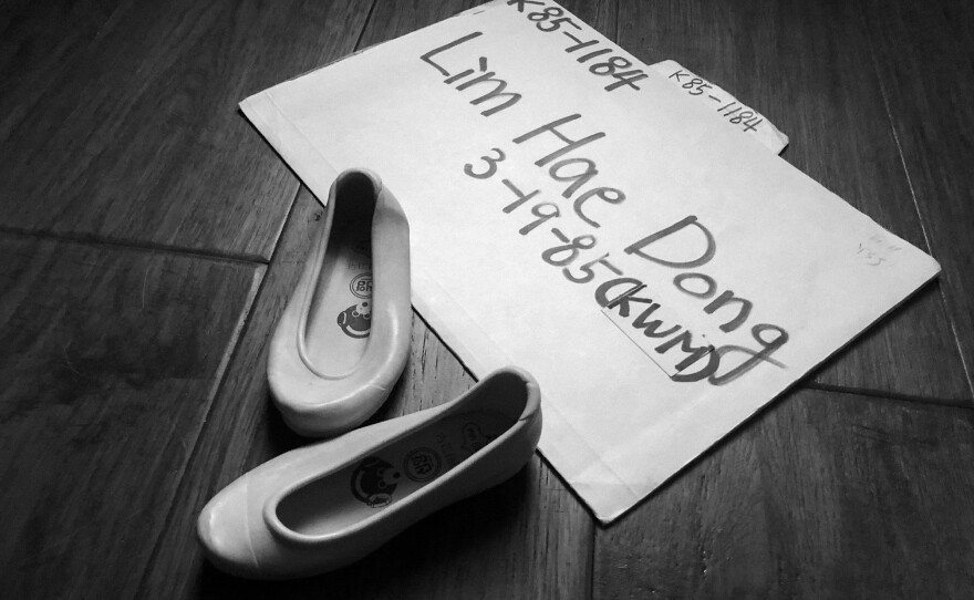 The shoes worn by Ian Morton as a baby when he came to the United States, displayed by his adoption folder, containing his health certificates and personal information from Korea.