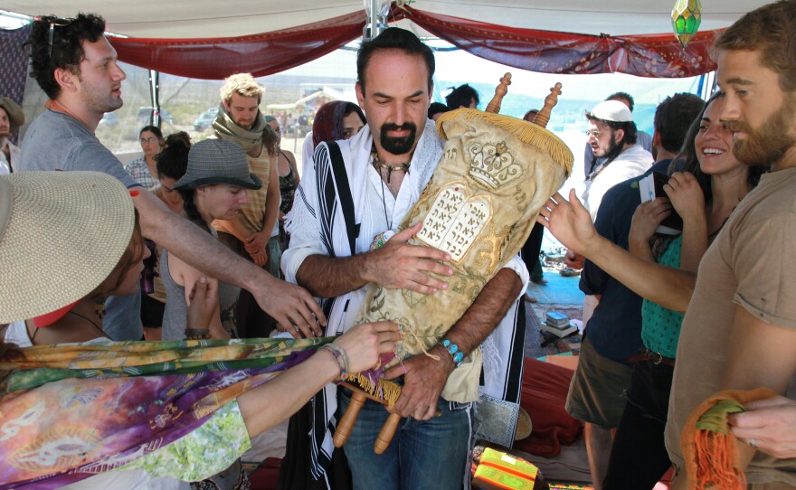 During a Saturday morning Shabbat service, Sagi Salomon carries a Torah scroll that survived the Holocaust through the Tent of Meeting. Touching the Torah cover appropriately is a symbolic way to show respect and affection for the Torah and the Jewish teachings it contains and represents.