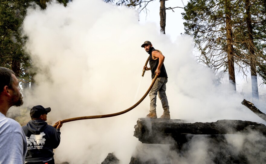 Derrick Harlan sprays water on a burn pile, Wednesday, Oct. 25, 2023, in Paradise, Calif. He was clearing a property of dead wood and flammable vegetation to meet the defensible space requirements Paradise adopted following the Camp Fire.