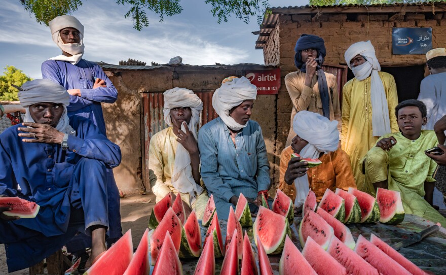 Young men eat slices of watermelon at a vendor's stall in a market in the village of Karnak, Chad. The village has seen Great Green Wall interventions from an nongovernmental group looking to plant acacia trees.