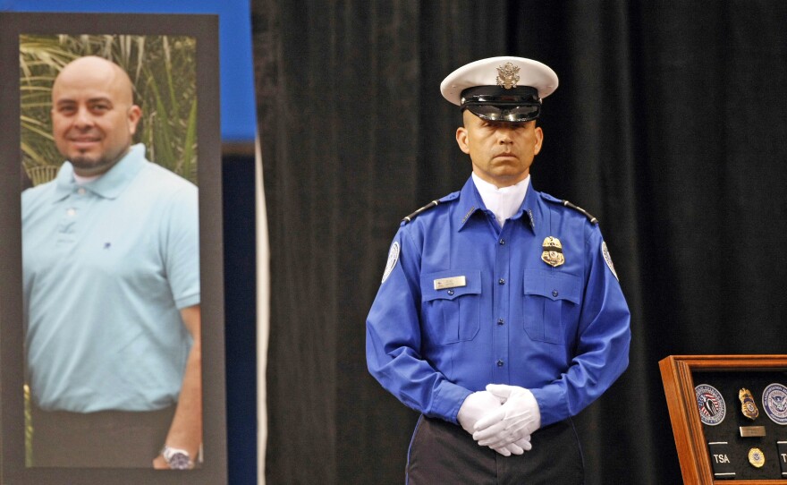 A Transportation Security Administration officer stands in front of a portrait of slain TSA officer Gerardo Hernandez during his public memorial in 2013 at the Los Angeles Sports Arena.