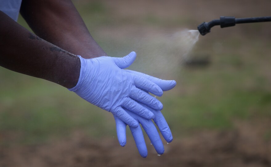 Protective equipment is in short supply. Here, a Liberian burial team carefully disinfects their gloves before disposing of them.