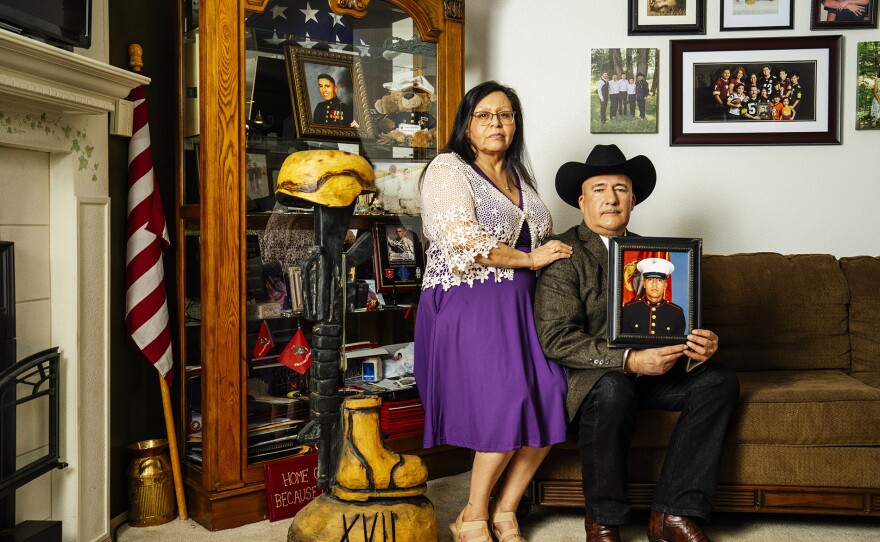 Adań (right) and Yolanda Gonzales are the parents of Sergeant Adań Gonzales, Jr., (seen in photo) a member of the 1st Battalion, 5th Marine Regiment, killed in action during Operation Enduring Freedom in Afghanistan on Aug. 7, 2011. Next to them is a curio cabinet filled with mementos of their son's service and a battlefield cross sculpture carved by chainsaw artist Anthony Marquez, a Marine veteran from Gonzales' unit. Marquez carved 17 such sculptures, all inscribed with the roman numeral XVII, for the 17 members of their unit killed in action. They are seen here in their home in Marysville, Washington, on Sat., April 13, 2024.
