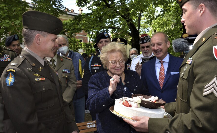Soldiers from U.S. Army Garrison Italy return a birthday cake to Meri Mion, center, in Vicenza, northern Italy, Thursday, April 28, 2022, to replace the one U.S. soldiers ate as they entered her hometown during one of the final battles of World War II. Mion, who turns 90 on Friday, wiped away tears as she was presented with the cake.