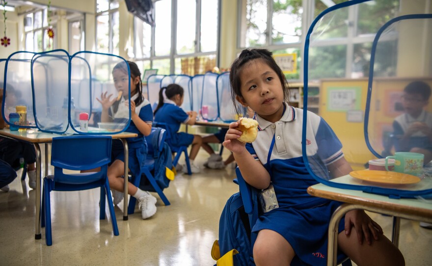 Kindergarten children eat their snacks behind plastic dividers at Tsung Tsin Primary School and Kindergarten.