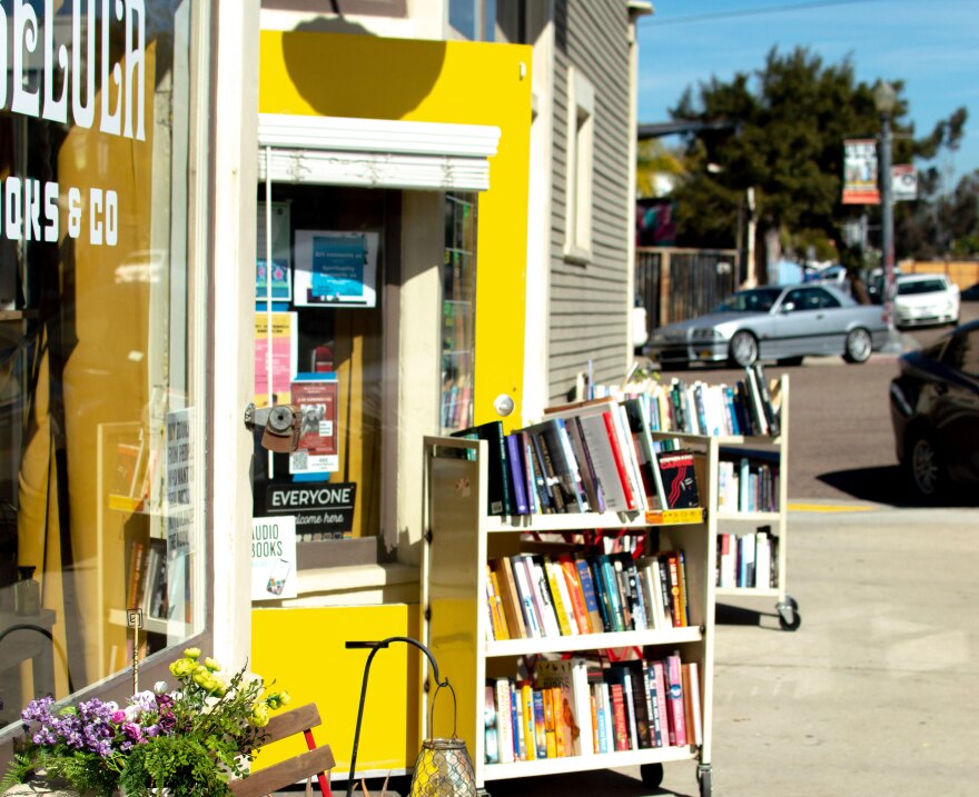 Libélula Books pictured from the sidewalk, with a yellow door and two carts of books outside.