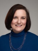 Woman smiling with short dark hair wearing a blue shirt.