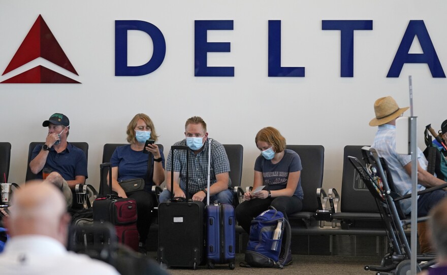 People sit under Delta sign at Salt Lake City International Airport on July 1, 2021. Delta Air Lines won't force employees to get vaccinated, but it's going to make unvaccinated workers pay a $200 monthly charge.