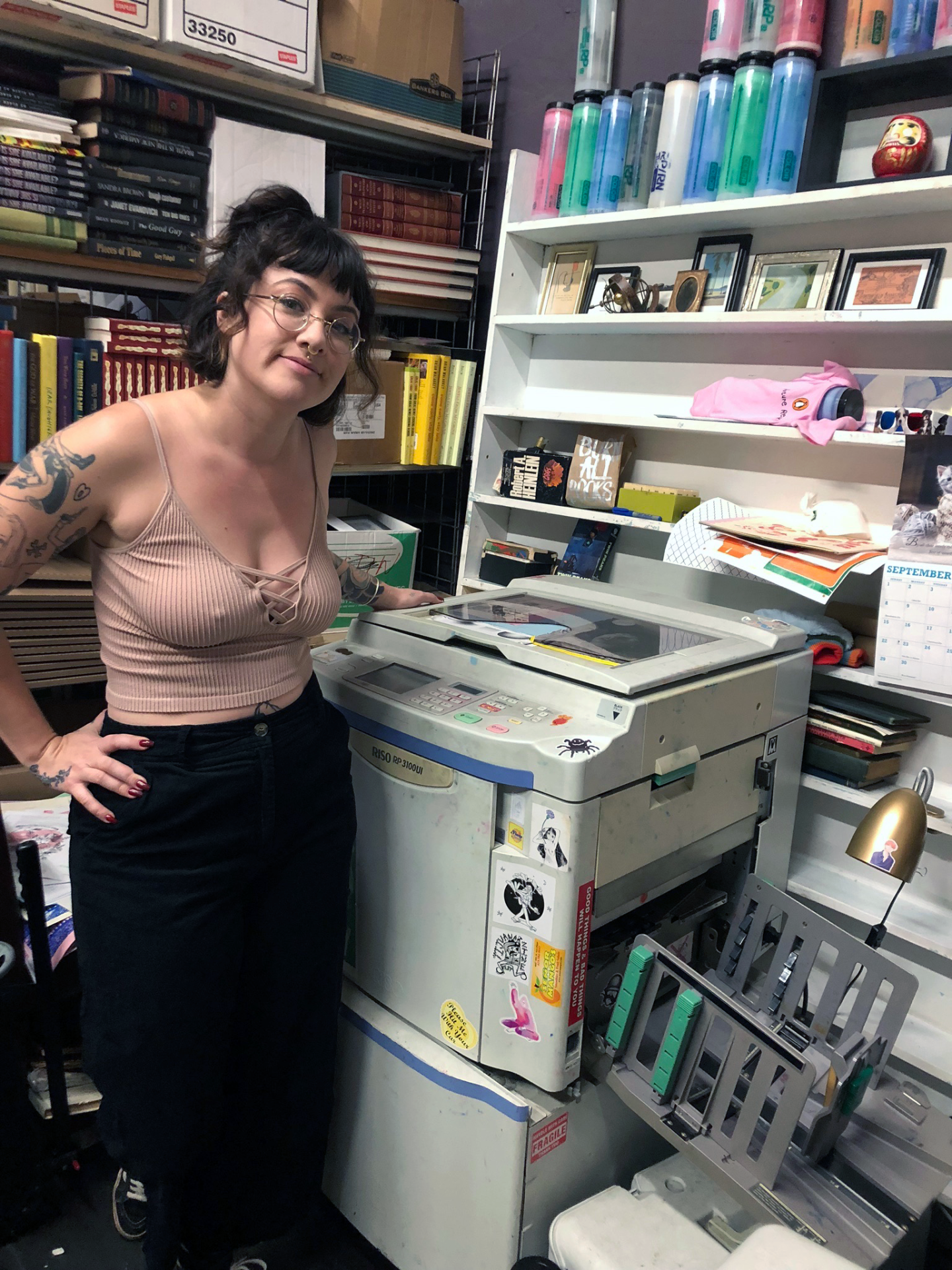 Burn All Books co-founder Manda Bernal stands beside a Riso printer.