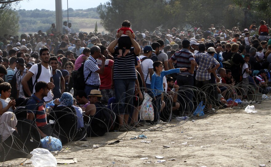 Migrants stand behind the barbed wire set by Macedonian police to stop thousands of migrants entering Macedonia illegally from Greece.