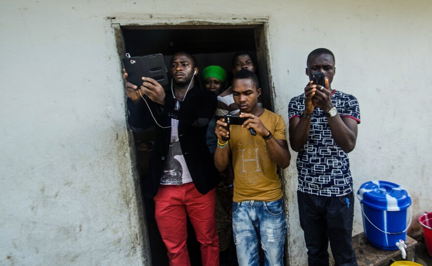 Locals photograph the body collector team. Family and friends have shunned its members, fearful that they might catch and pass on Ebola.